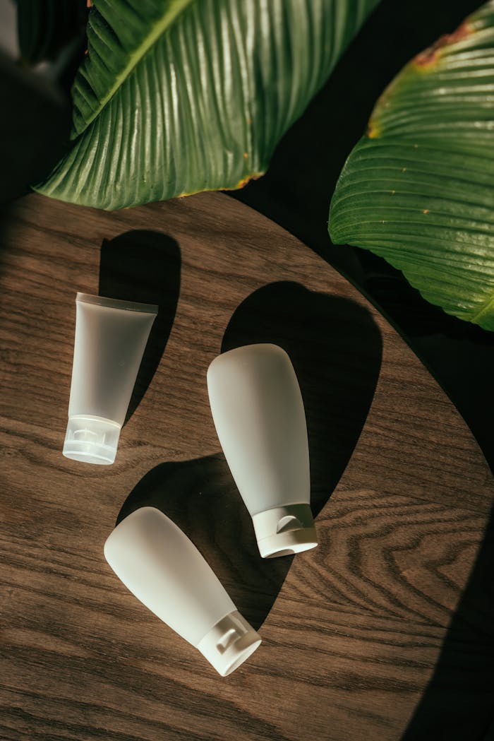 Minimalist cosmetic bottles placed on a wooden table surrounded by green leaves.