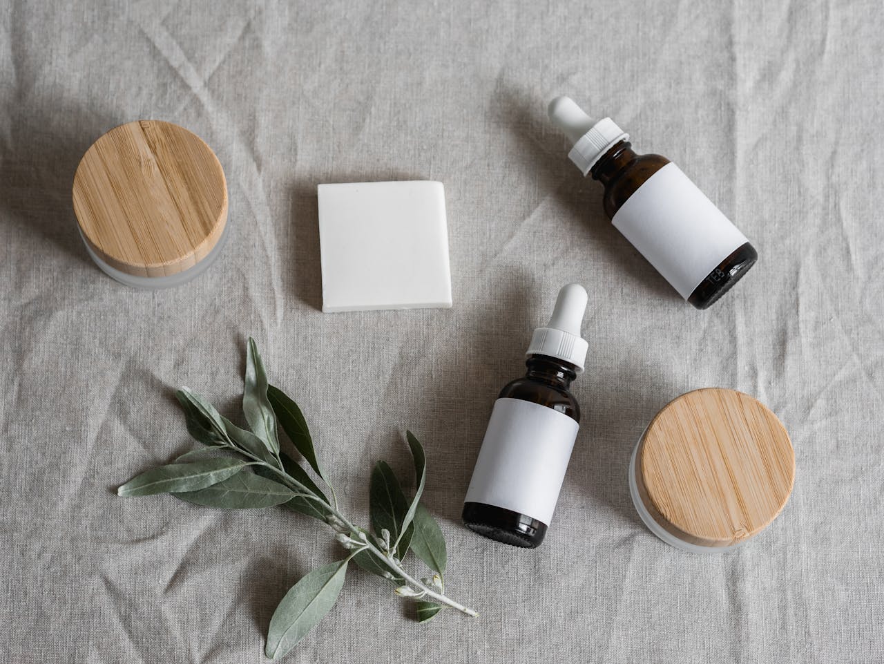 Top view of skincare products with a natural theme, featuring bottles, jars, and a plant on linen cloth.