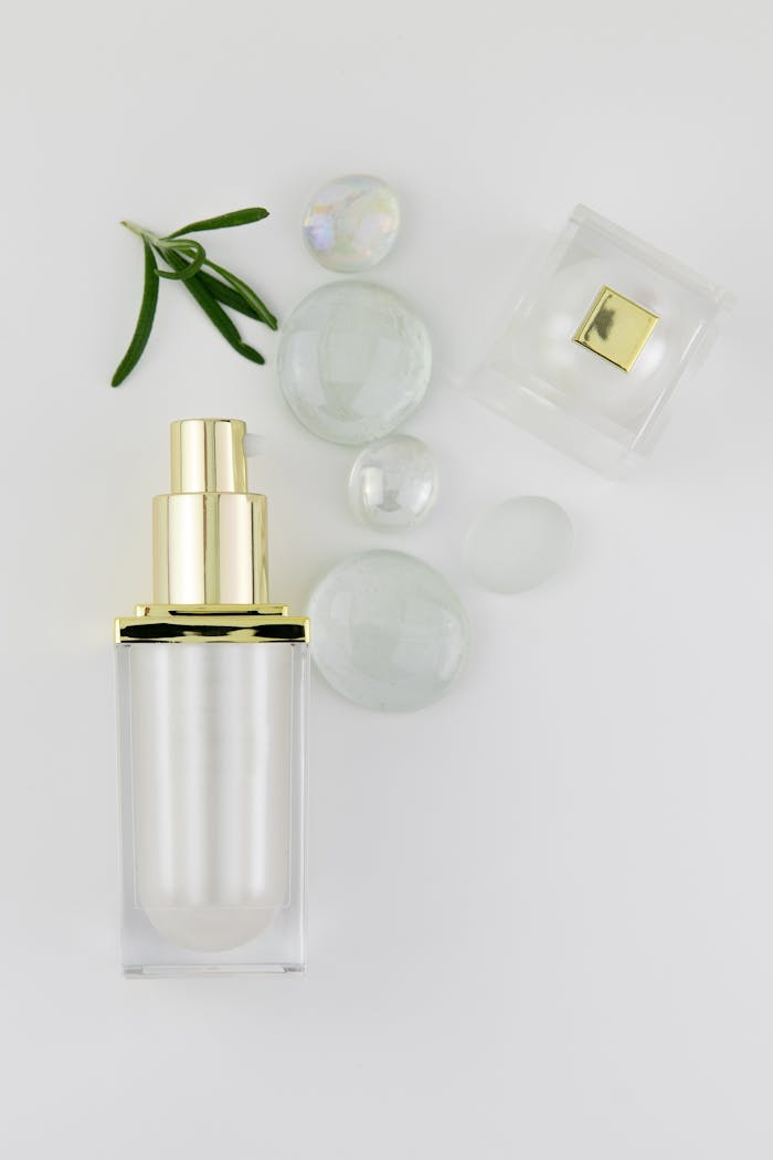 A minimalist aesthetic featuring a perfume bottle with glass lid, crystals, and leaves on a white background.